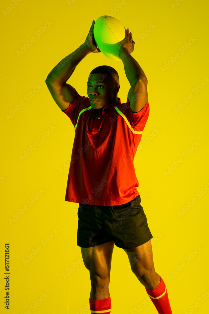 非裔美国男子橄榄球运动员在黄色灯光下拿着橄榄球