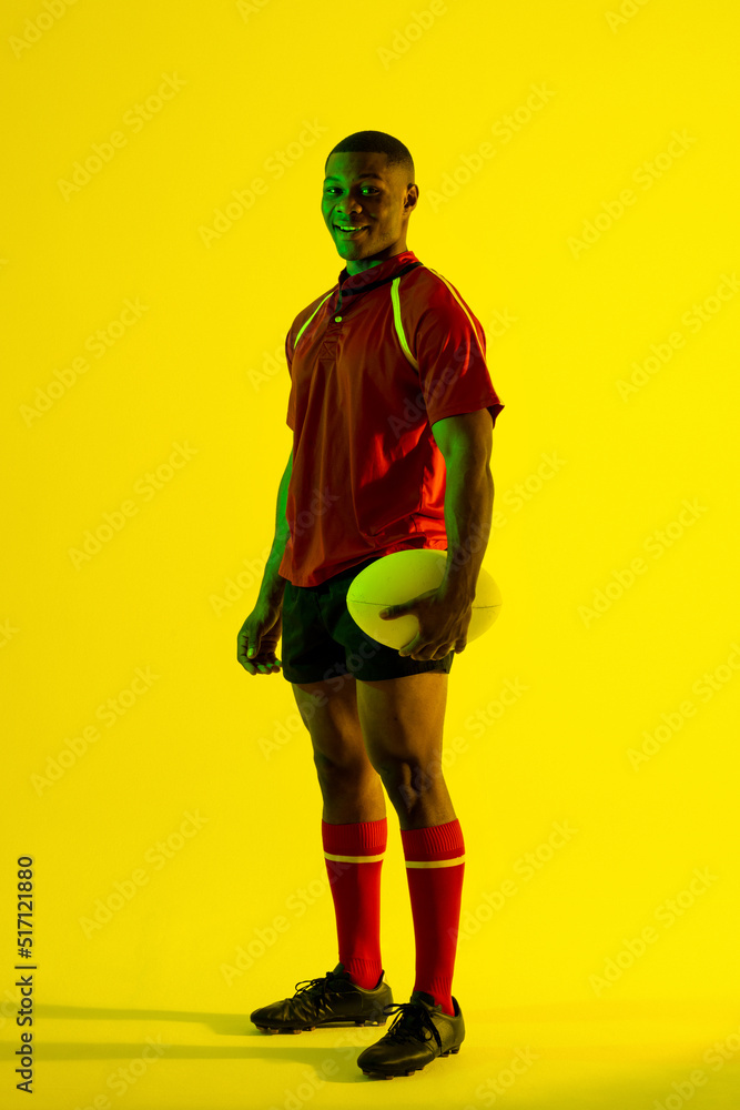 快乐的非裔美国男子橄榄球运动员在黄色灯光下拿着橄榄球的肖像