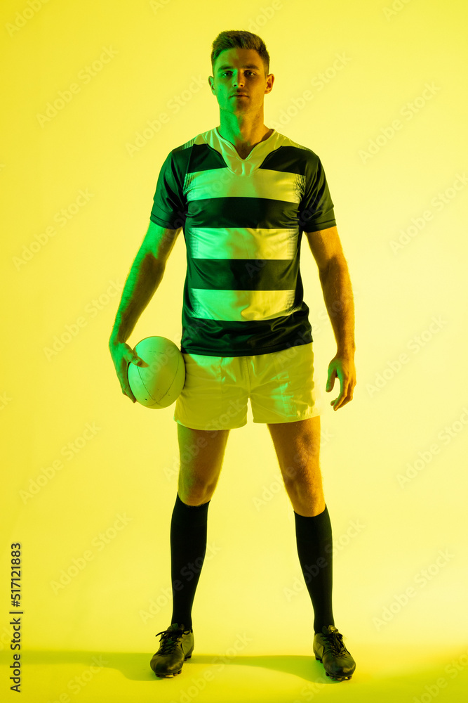 黄色灯光下拿着橄榄球的高加索男子橄榄球运动员的肖像