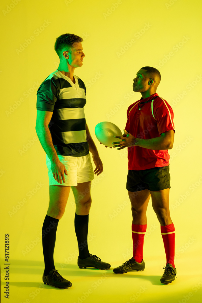 多样化的男性橄榄球运动员在黄色灯光下拿着橄榄球