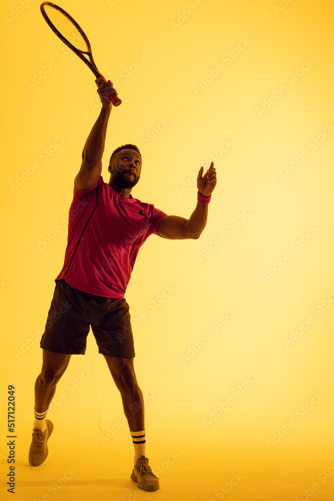 非裔美国男子网球运动员在黄色灯光下击球的垂直图像