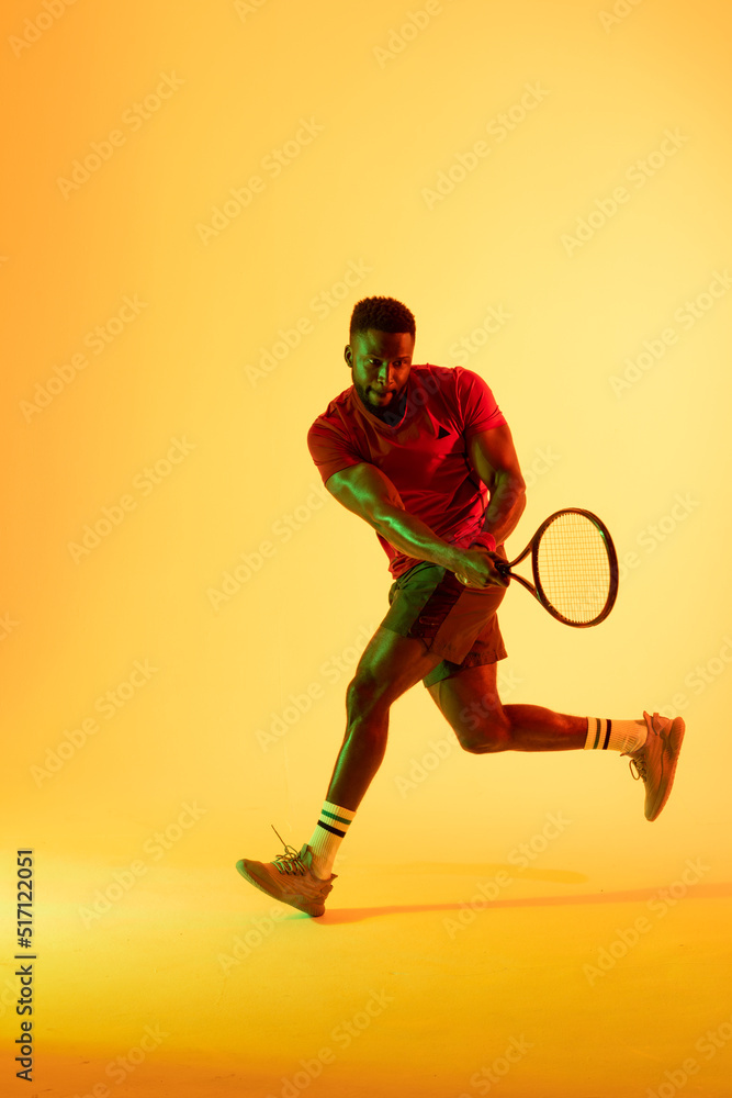 非裔美国男子网球运动员在黄色灯光下击球的垂直图像