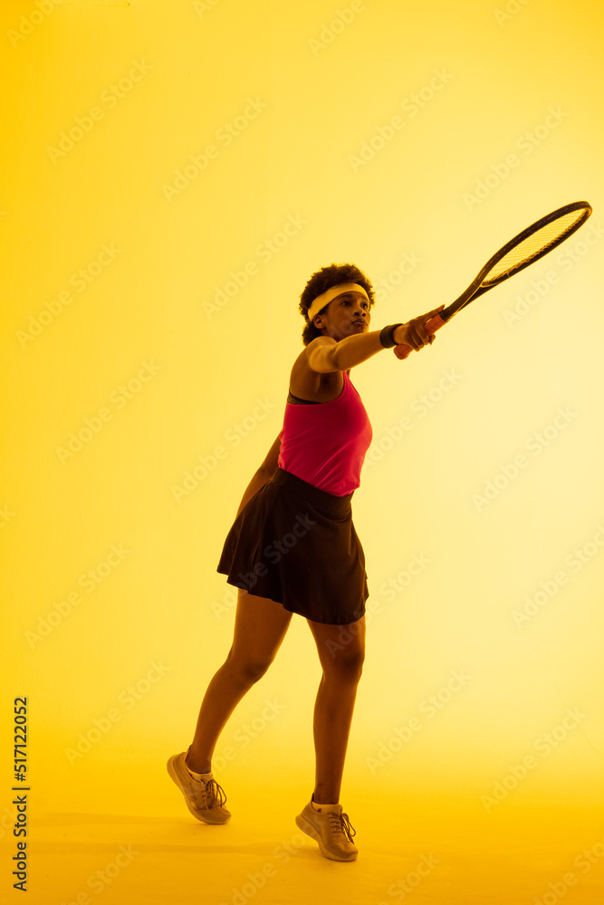 非裔美国女网球运动员在黄色灯光下击球的垂直图像