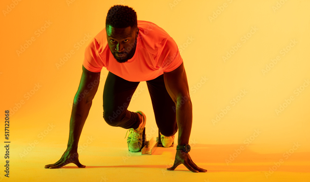 非裔美国男运动员在黄色灯光下准备跑步的照片