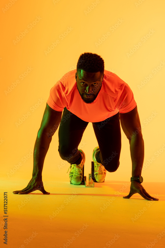 非裔美国男运动员在黄色灯光下准备跑步的垂直图像