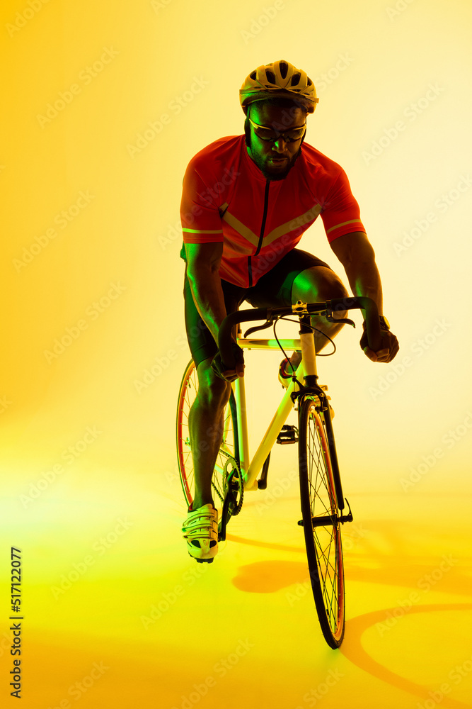 Vertical image of african american male cyclist riding bike in yellow lighting