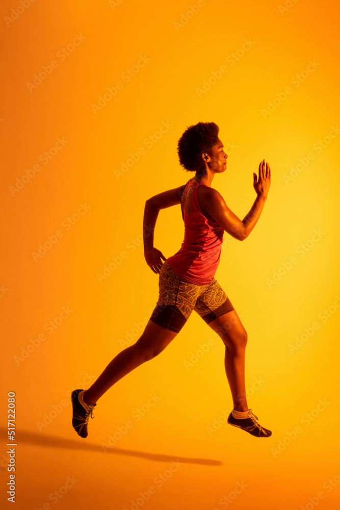非裔美国女运动员在霓虹橙色灯光下奔跑的垂直图像