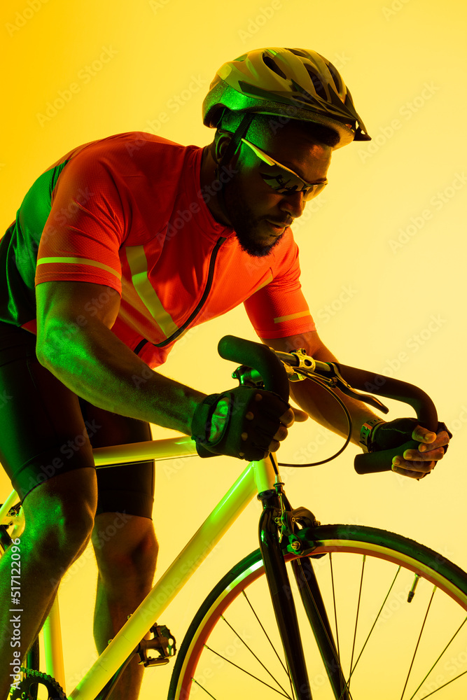 在黄色灯光下骑自行车的非裔美国男性自行车手的垂直图像