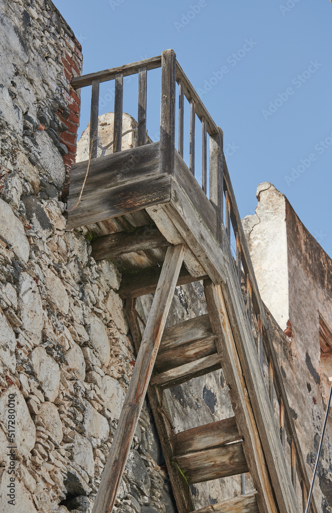 在蓝天背景下，通往一座历史建筑屋顶的旧木楼梯。Weat