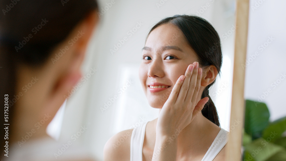 年轻的亚洲女性触摸健康的面部皮肤照镜子