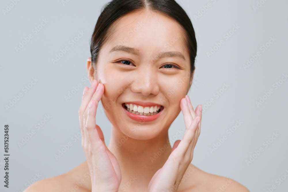 描绘一位年轻的亚洲女性在灰色背景下触摸健康的面部美容皮肤。