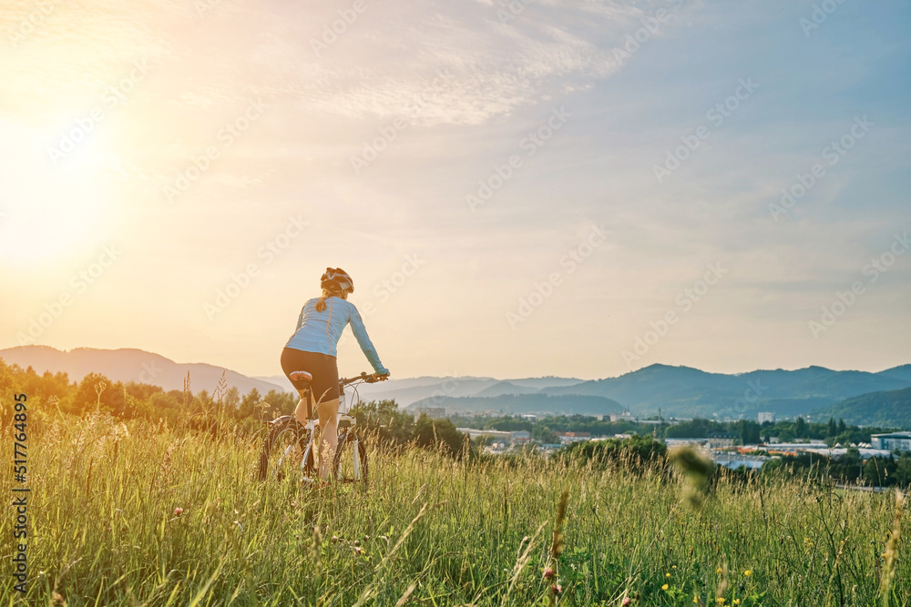 骑自行车的女人戴着头盔在阳光明媚的日子里在森林里的一座山上进行户外运动。Si