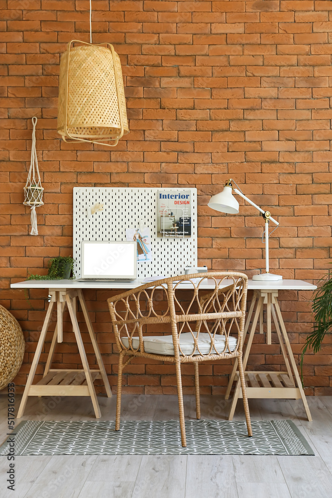 Modern workplace with peg board, laptop and lamp near brick wall
