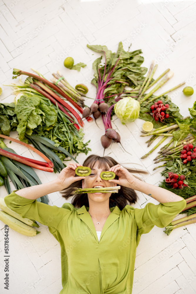 Portrait of a young cheerful woman with lots of fresh vegetables, fruits and greens above her head, 