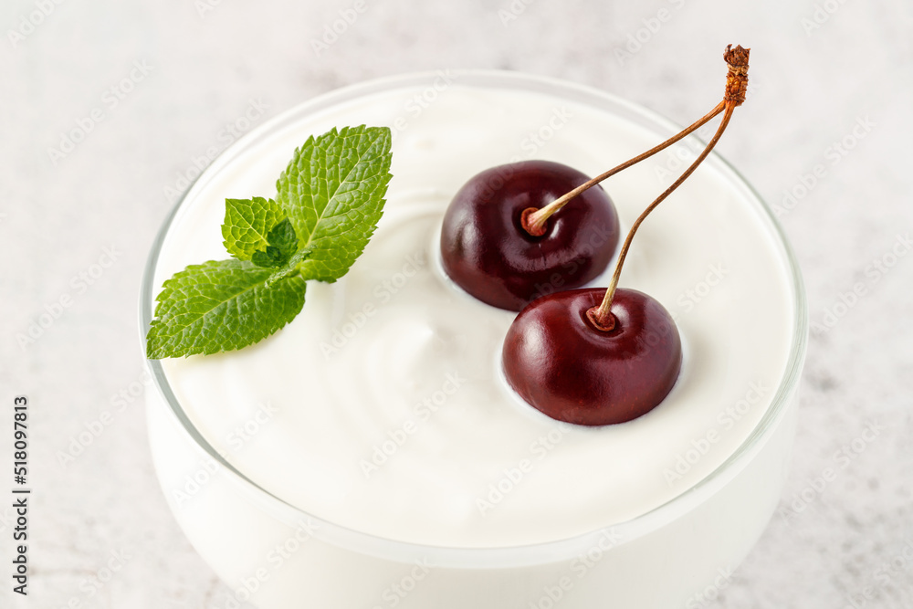 牛奶布丁或酸奶，配成熟的樱桃浆果和薄荷叶，放在玻璃碗里，在灯光下特写