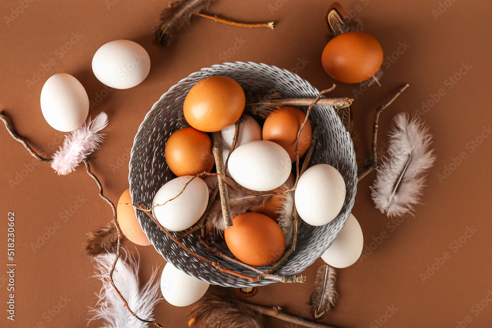 彩色背景上有鸡蛋、羽毛和树枝的柳条碗