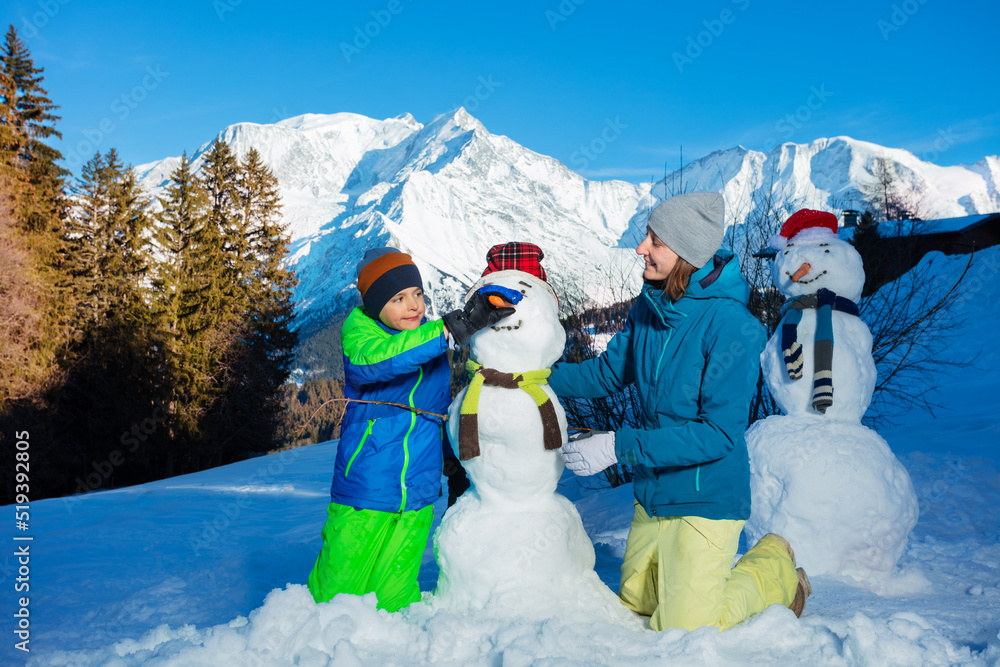 Family fun mother and a boy build snowman with in scarf, carrot
