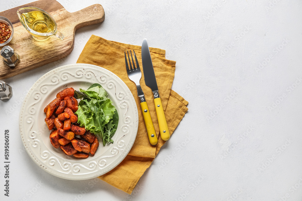 一盘美味的烤胡萝卜，配绿色蔬菜和餐具，背景为浅色