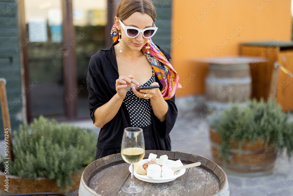 一名妇女在意大利马雷马地区当地的农场商店品尝奶酪和葡萄酒时使用手机。康塞