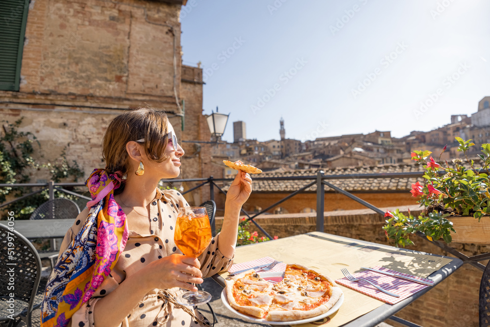 年轻女子在户外餐厅享用披萨和葡萄酒的午餐，可以欣赏到古老的美景