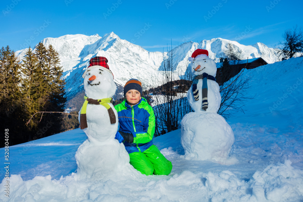 男孩坐在山上玩新堆的雪人