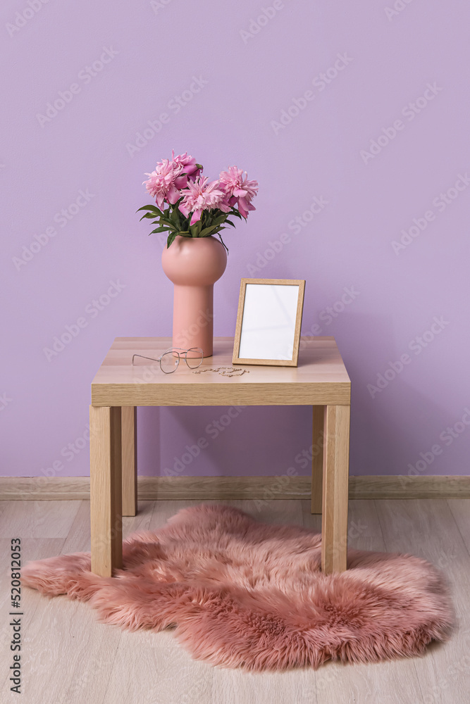 彩色墙壁附近的桌子上放着一个花瓶，花瓶里有一束牡丹花、空白相框和女性配饰