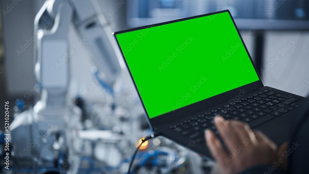 黑人女工程师在现场使用带绿屏显示屏的笔记本电脑编程机器人手臂