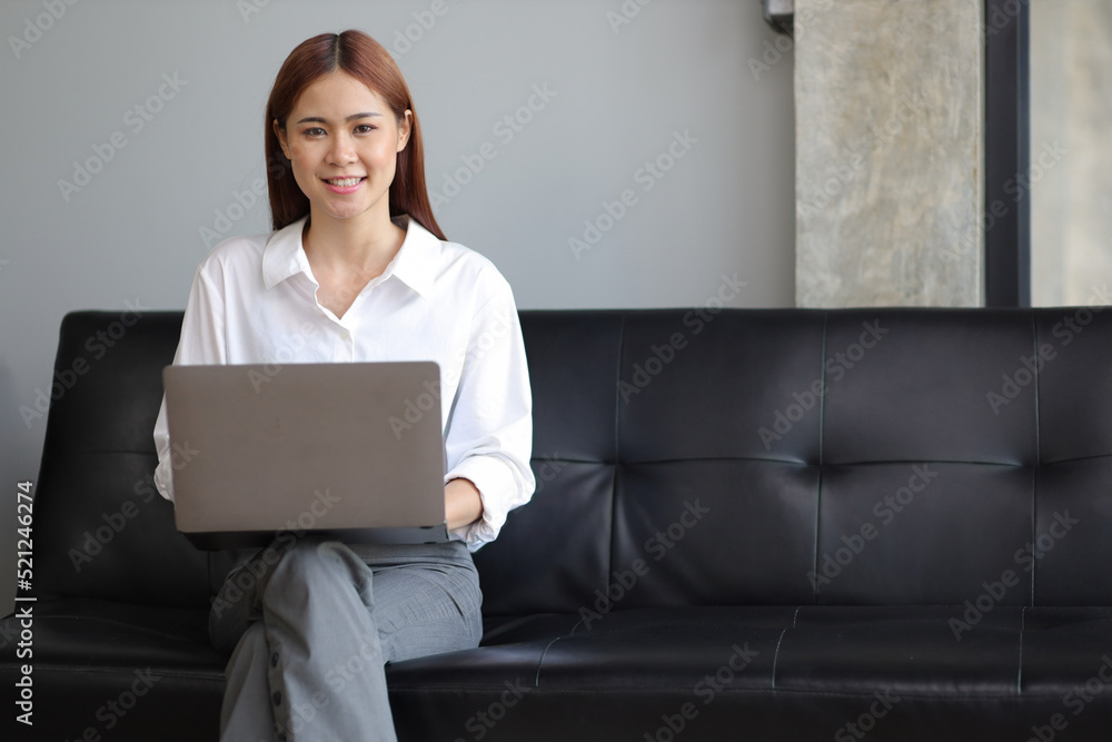 亚洲女人坐在沙发上，在家里用笔记本电脑的肖像。在家网上购物。
