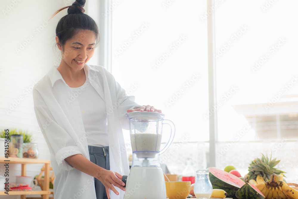 An Asian woman is making a fruit yogurt smoothie in her kitchen with ingredients such as watermelon,