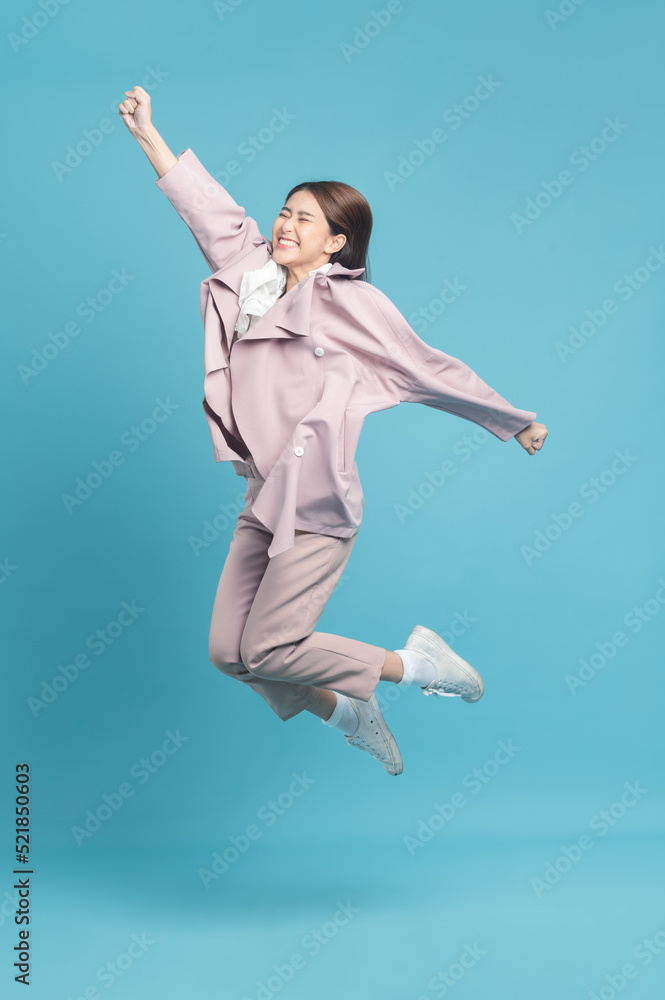 年轻漂亮的亚洲女人穿着时髦的休闲布，穿着粉色外套，兴奋地跳跃