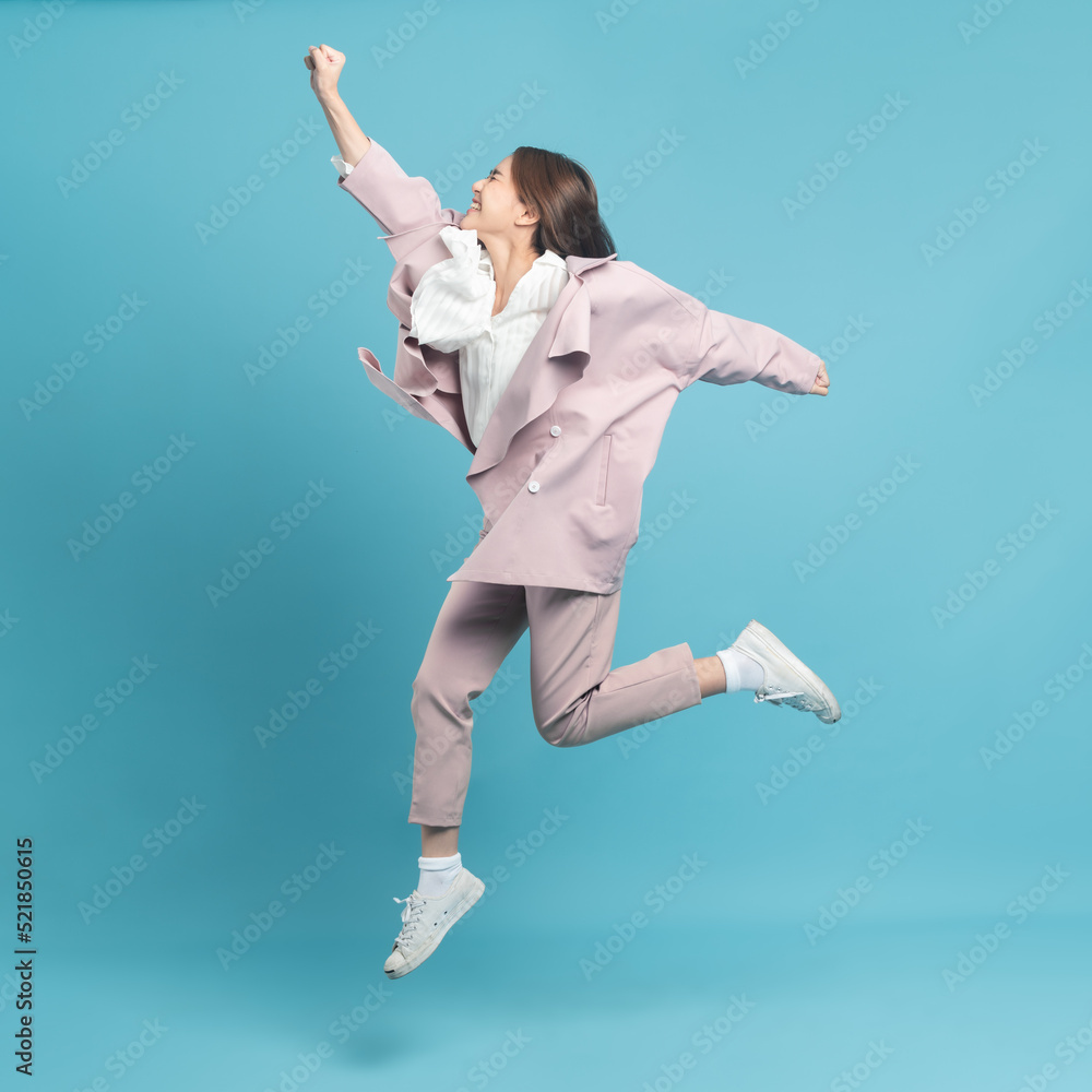 年轻漂亮的亚洲女人穿着时髦的休闲布，穿着粉色外套，兴奋地跳跃