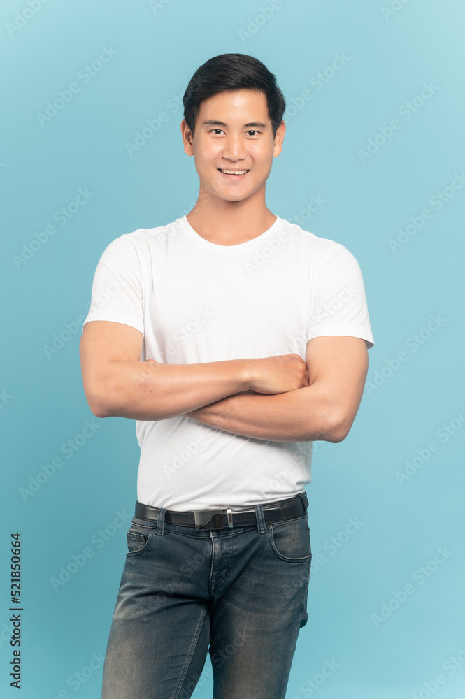 漂亮的亚洲小伙子，穿着白色t恤和牛仔裤，蓝色背景隔离