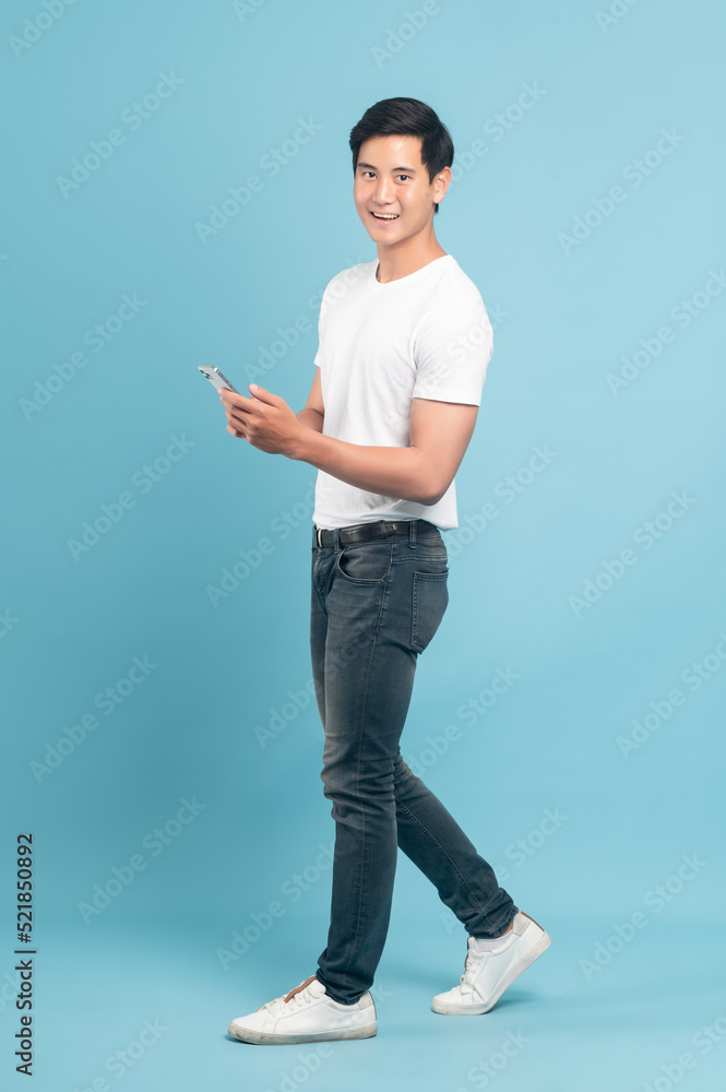 一个穿着白色t恤和牛仔裤、拿着蓝色背景隔离智能手机的亚洲好人