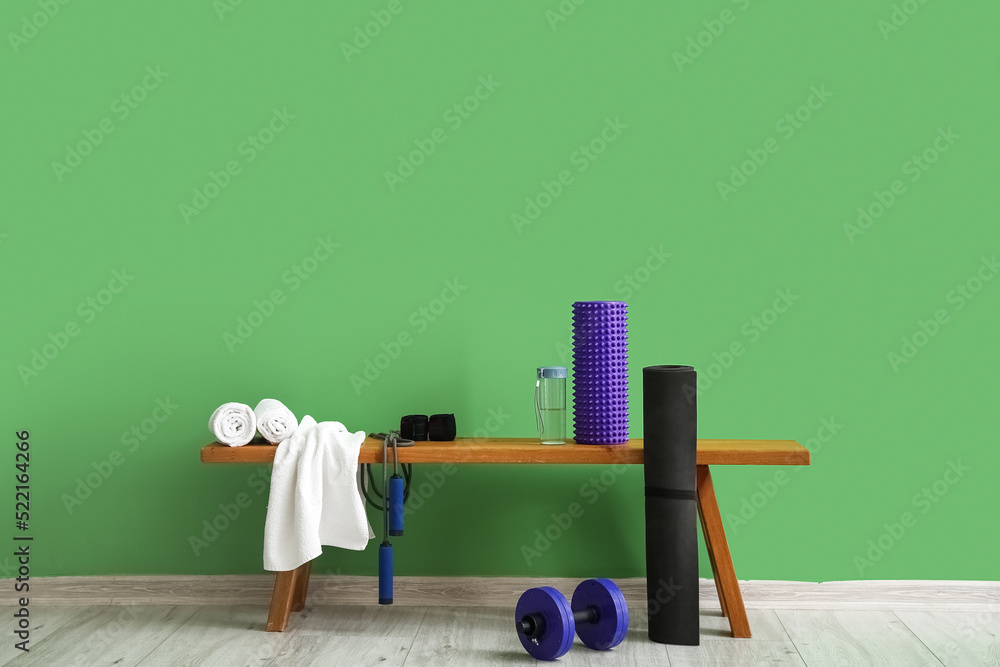 Bench with sports equipment and bottle of water near green wall