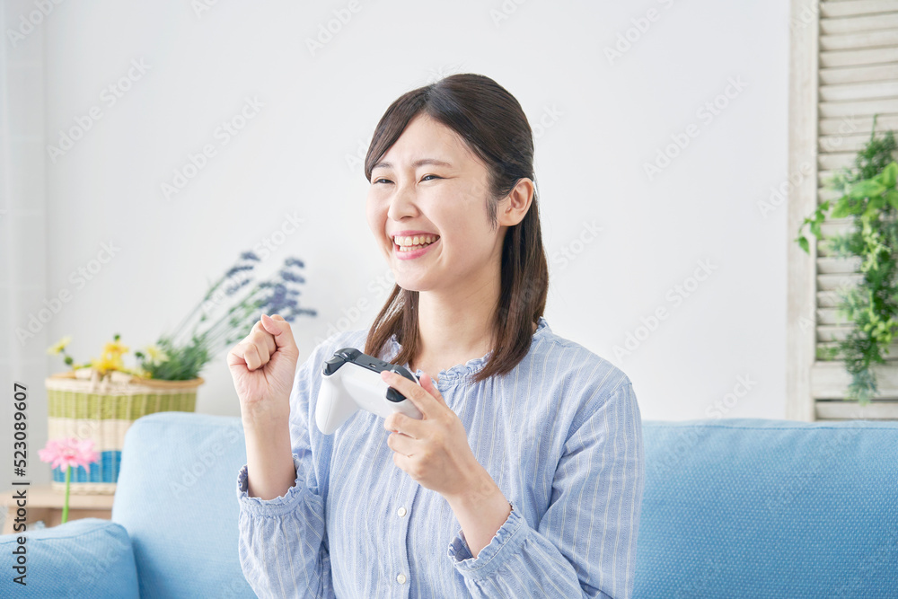自宅で一人でテレビゲームをしてガッツポーズをする女性