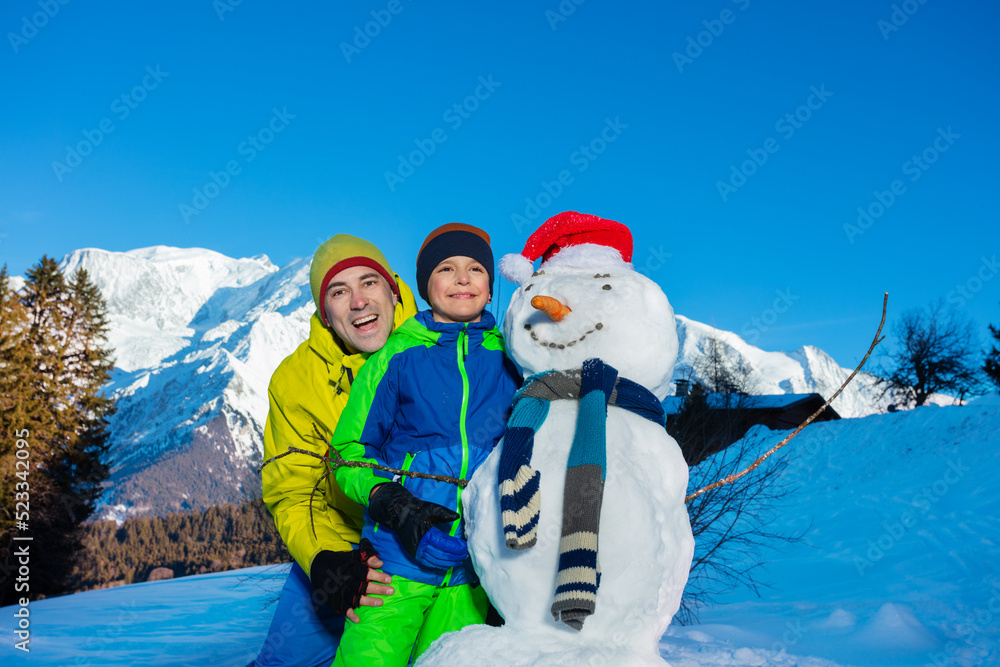 Boy and dad playing with newly made snowman in the mountains
