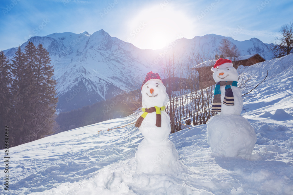 Two snowmen with carrot hat and scarf over mountains