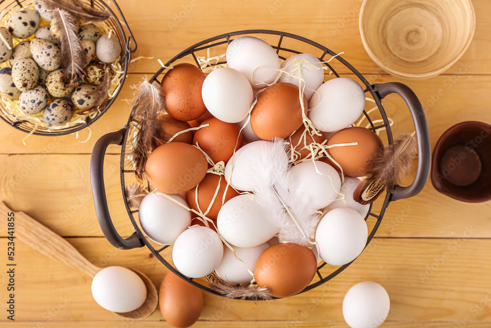 Basket of fresh chicken eggs and feathers on wooden background