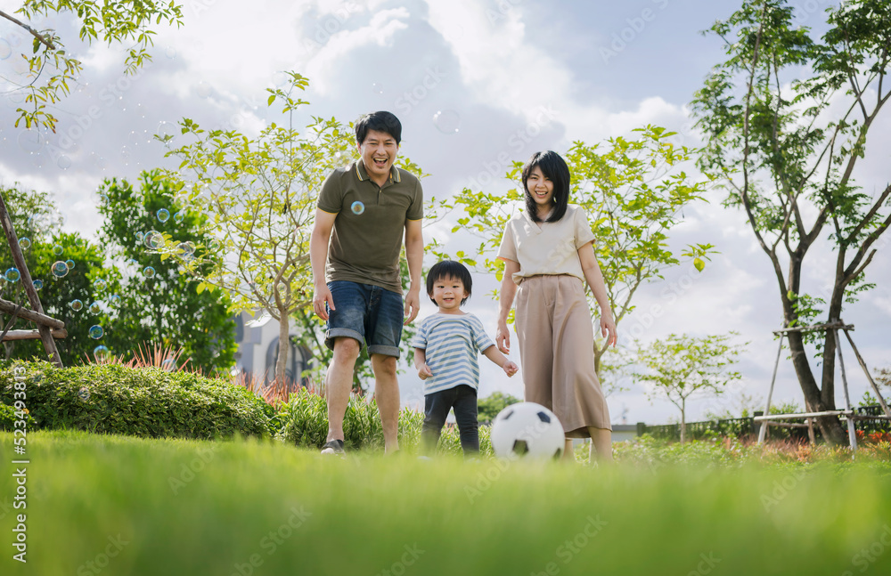 亚洲父母和小男孩一起在公园踢足球。幸福的家庭生活理念。