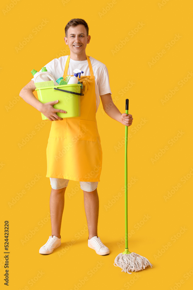 Smiling young man with cleaning supplies on yellow background