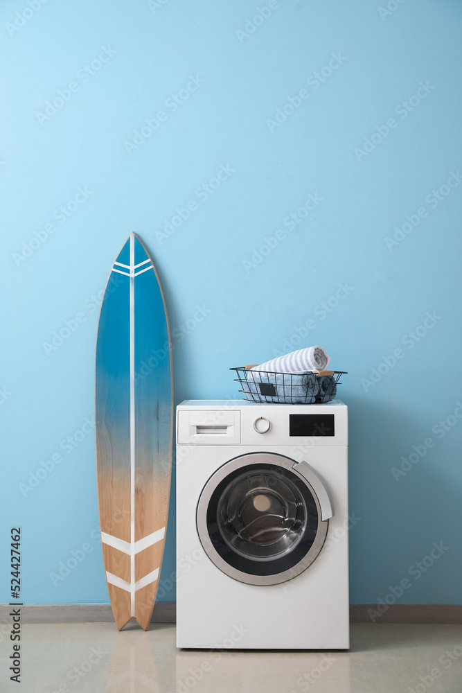 洗衣机上有毛巾的篮子，靠近蓝墙的冲浪板
