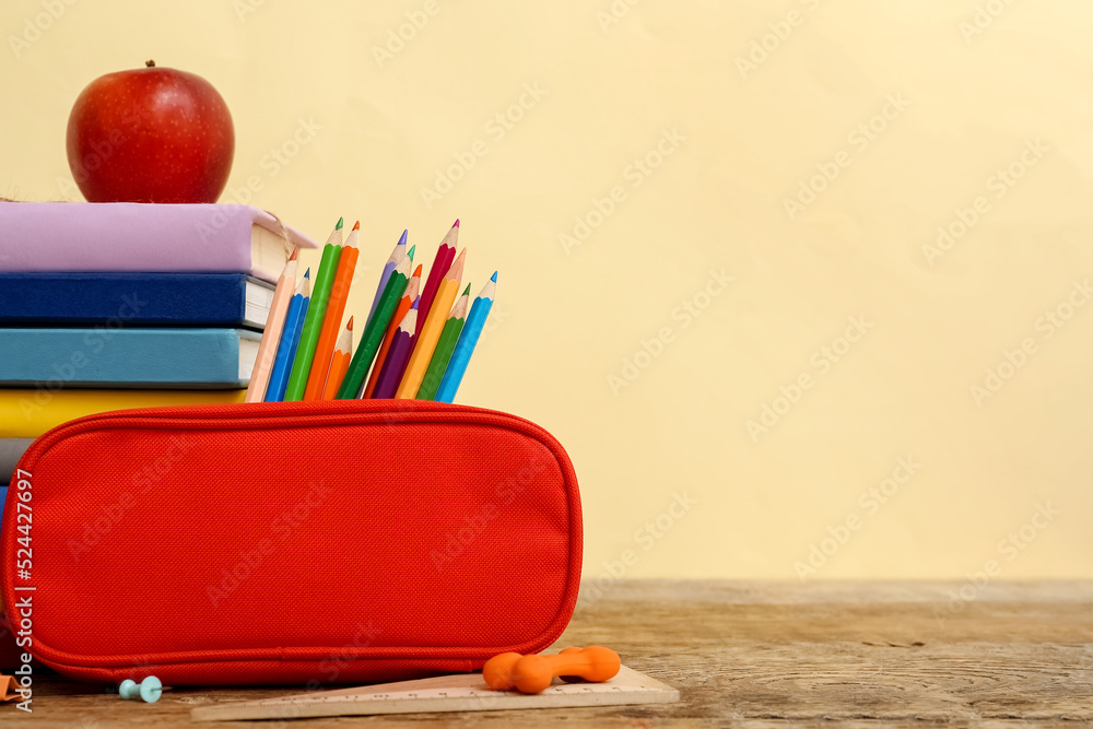 米色背景下桌上放着学校文具和苹果的红色铅笔盒