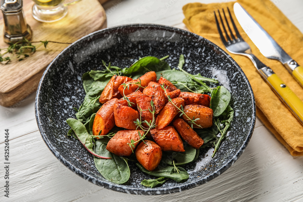 一盘美味的烤胡萝卜配绿色蔬菜，放在浅色木桌上，特写