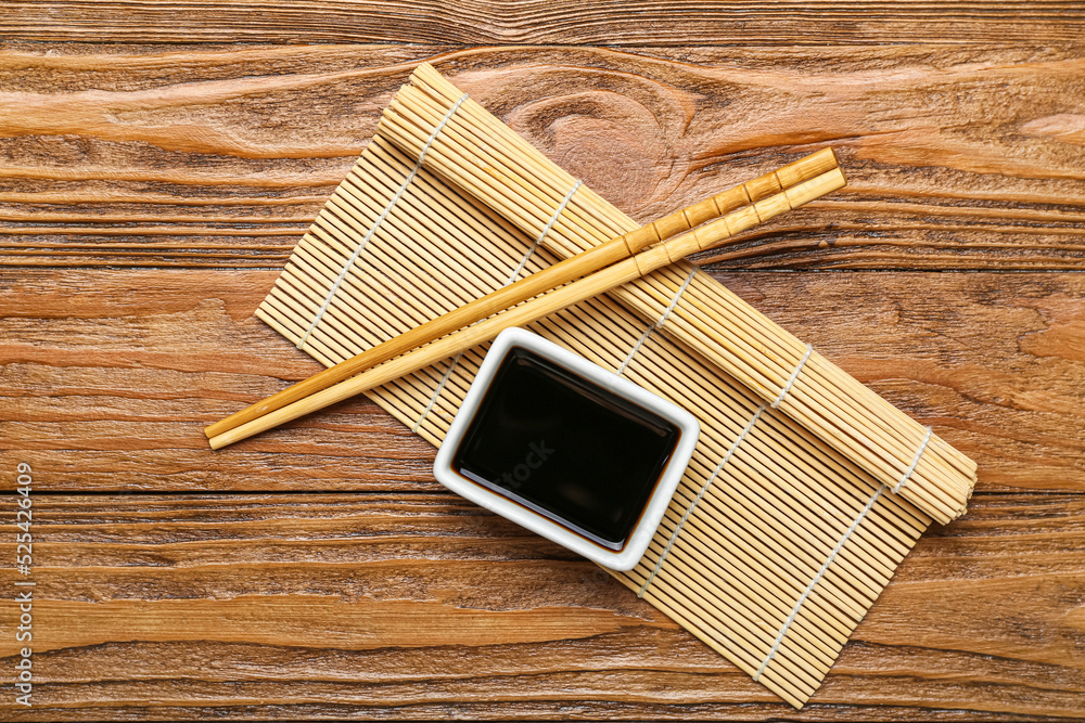 Bowl of soy sauce, chopsticks and bamboo mat on wooden background