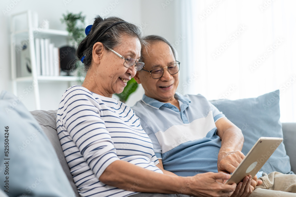 亚洲老年男性和女性在家中手持和使用平板电脑。