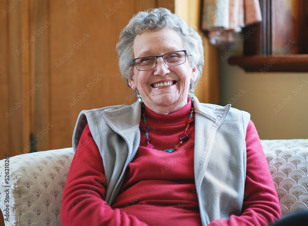 幸福的老妇人微笑着坐在家里的沙发上享受退休生活