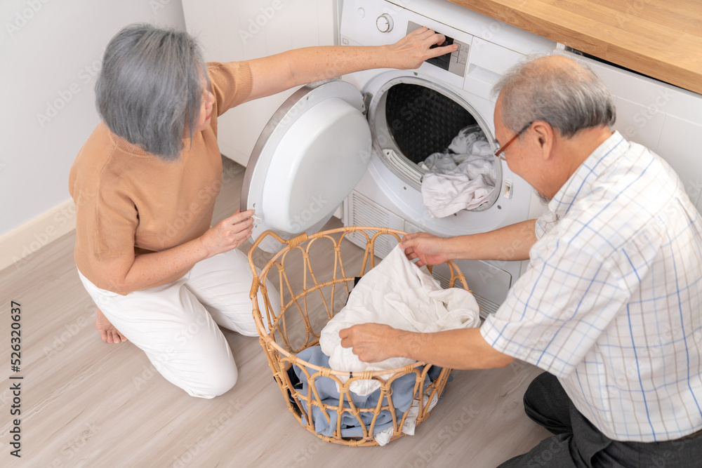 Senior couple working together to complete their household chores at the washing machine in a happy 