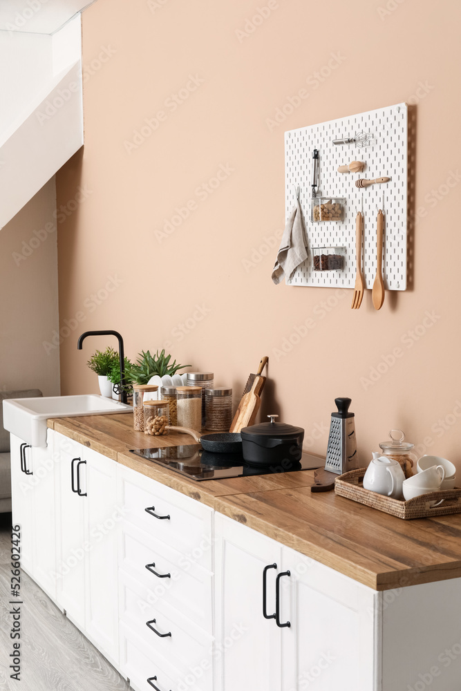 Interior of stylish kitchen with white counters, utensils and pegboard