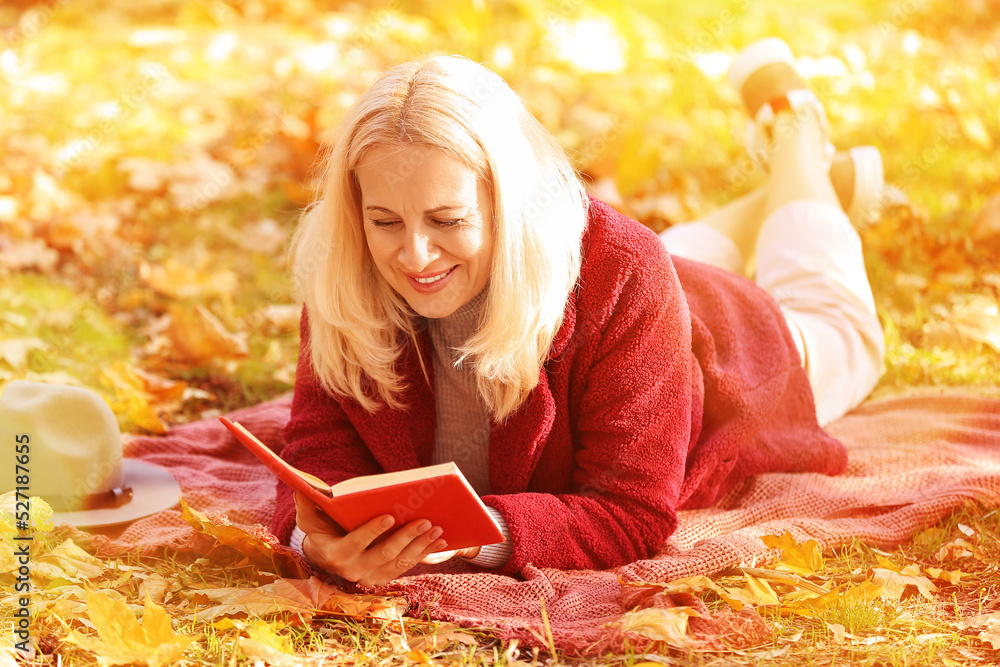 成熟的女人在秋天的公园里读格子书