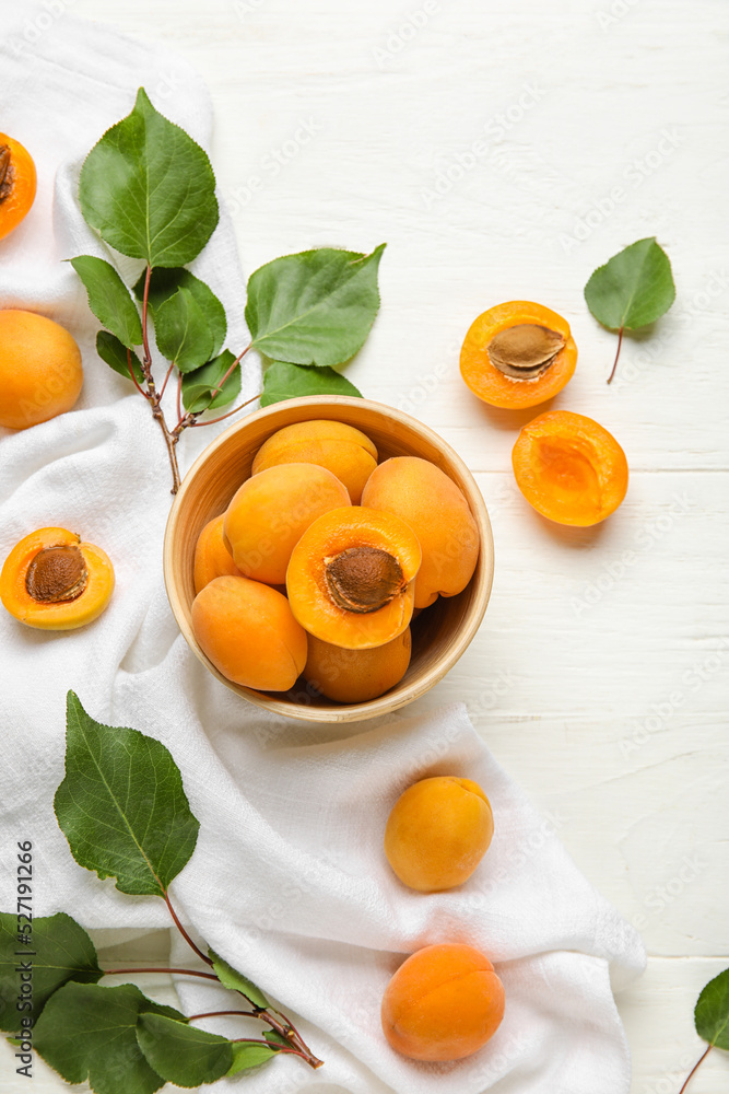 Composition with bowl of ripe apricots and green leaves on light wooden background